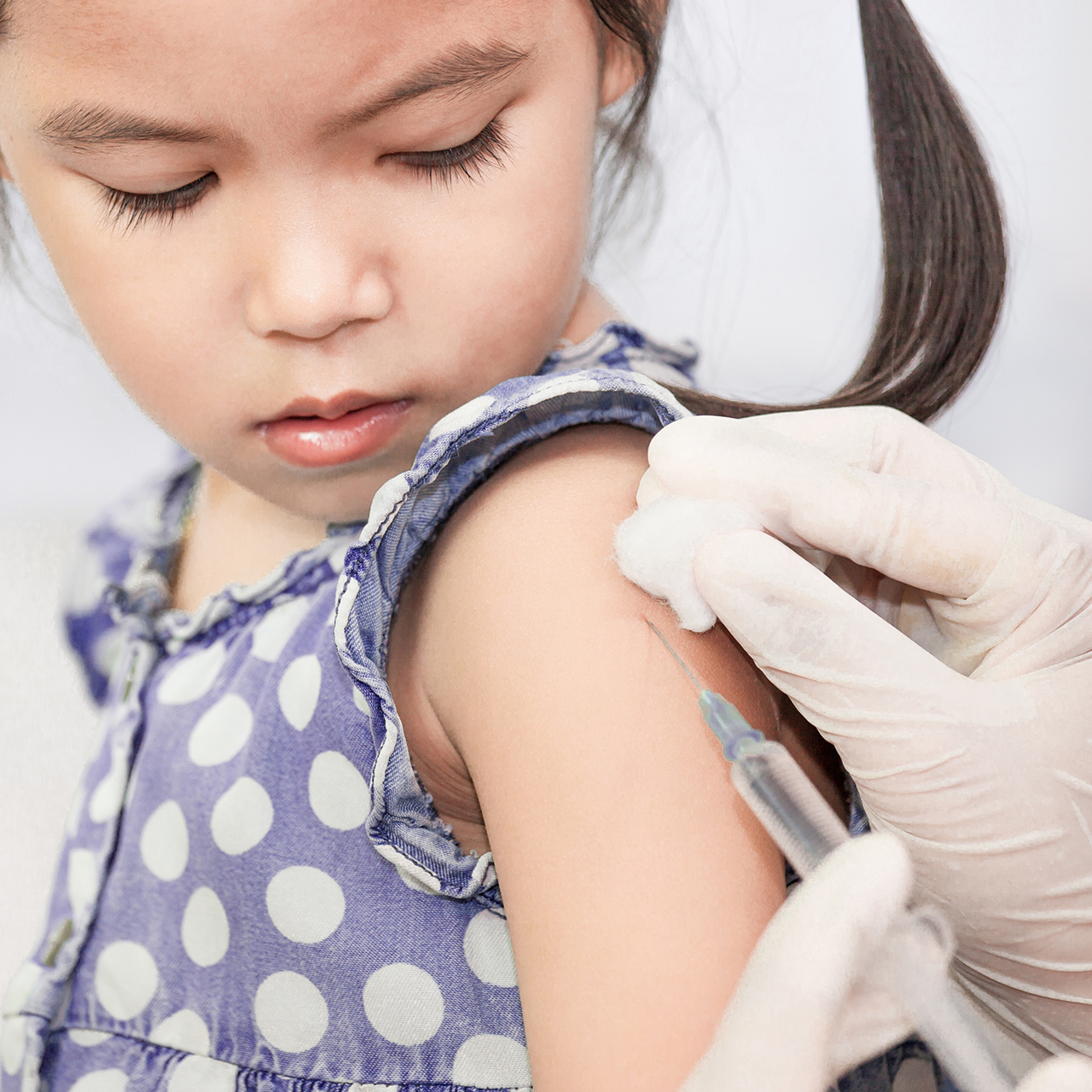 A young girl watches as she is given an injection via syringe and needle.